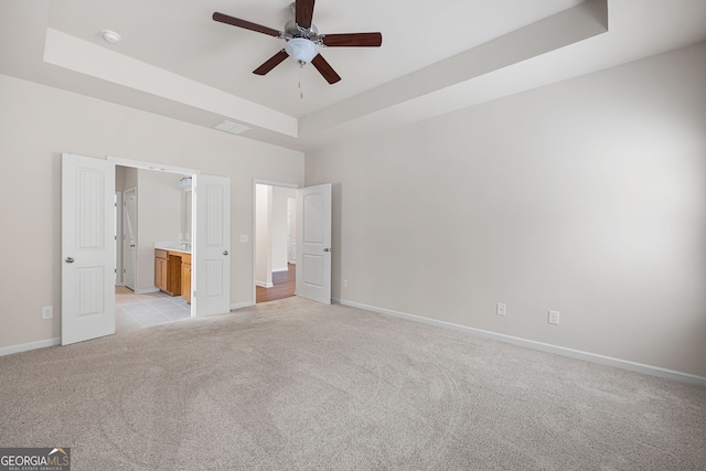 131 Prominence Ct, Canton, GA 30114 - unfurnished bedroom featuring a tray ceiling, light colored carpet, baseboards, ensuite bathroom, and a ceiling fan