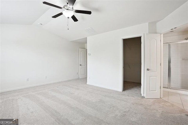 unfurnished bedroom with light carpet, a spacious closet, vaulted ceiling, baseboards, and ceiling fan
