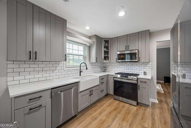 kitchen with stainless steel appliances, gray cabinets, a sink, light wood-style flooring, and light countertops