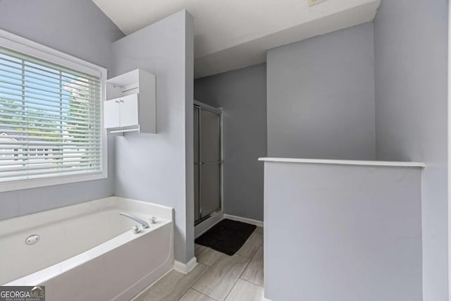 bathroom featuring a shower stall, a bath, and baseboards