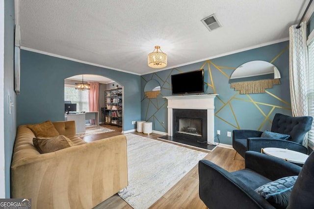 living room featuring ornamental molding, arched walkways, wood finished floors, a fireplace, and baseboards