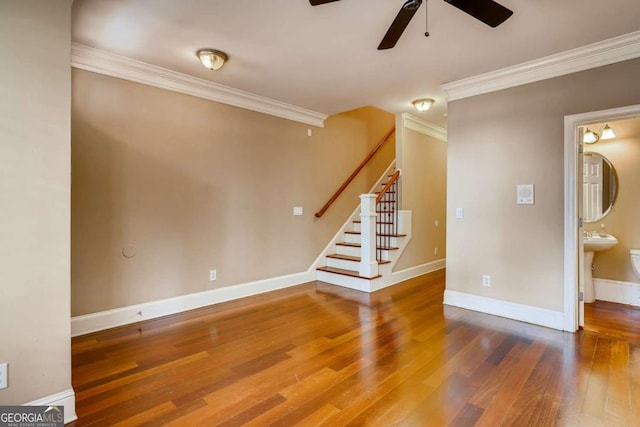unfurnished living room with a ceiling fan, ornamental molding, wood finished floors, baseboards, and stairs