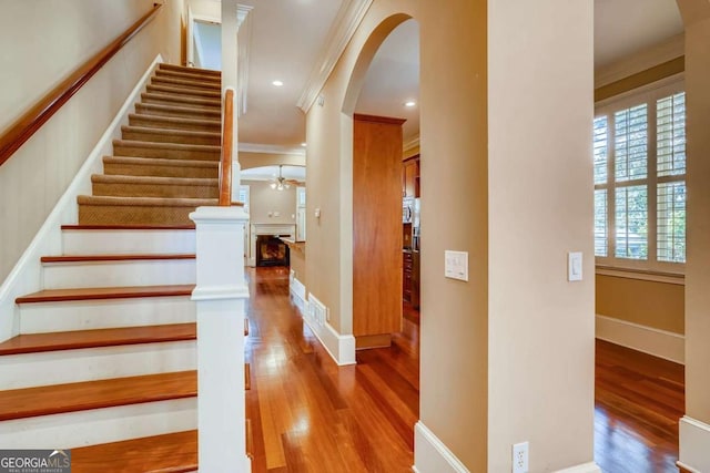staircase featuring wood finished floors, arched walkways, ornamental molding, baseboards, and a fireplace