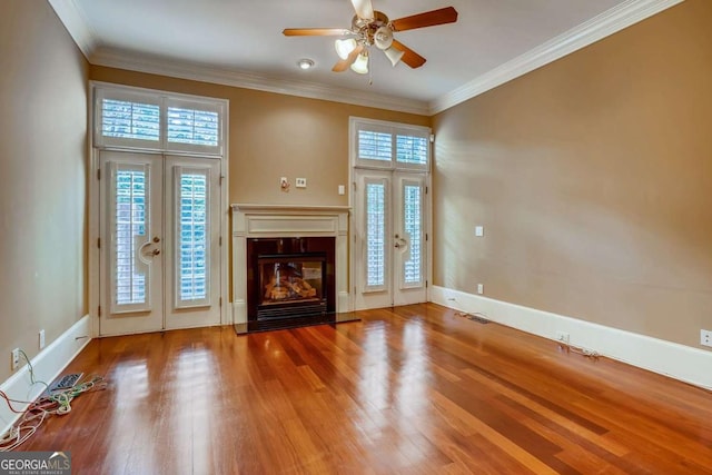 unfurnished living room featuring a fireplace with flush hearth, wood finished floors, ceiling fan, french doors, and ornamental molding