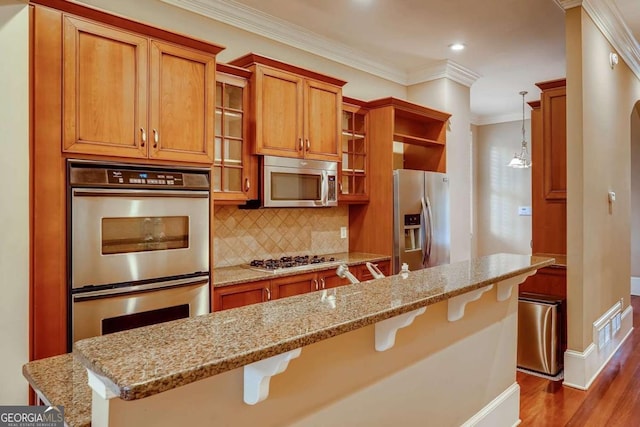 kitchen with stainless steel appliances, brown cabinets, a breakfast bar area, backsplash, and dark wood-type flooring