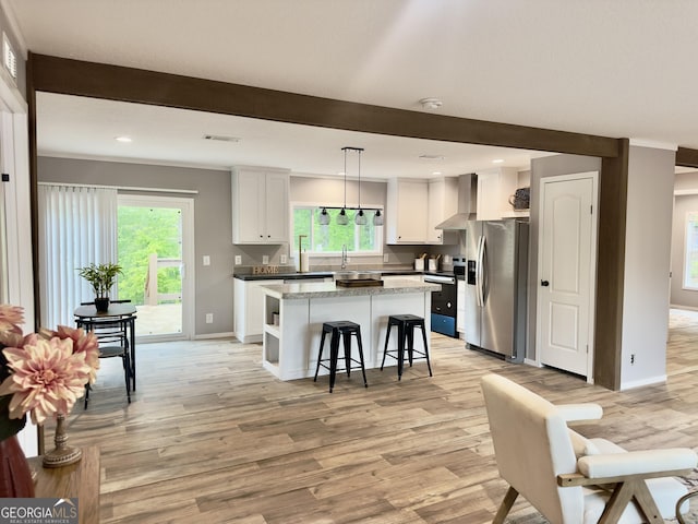 kitchen with appliances with stainless steel finishes, wall chimney exhaust hood, a kitchen island, light wood-type flooring, and white cabinetry