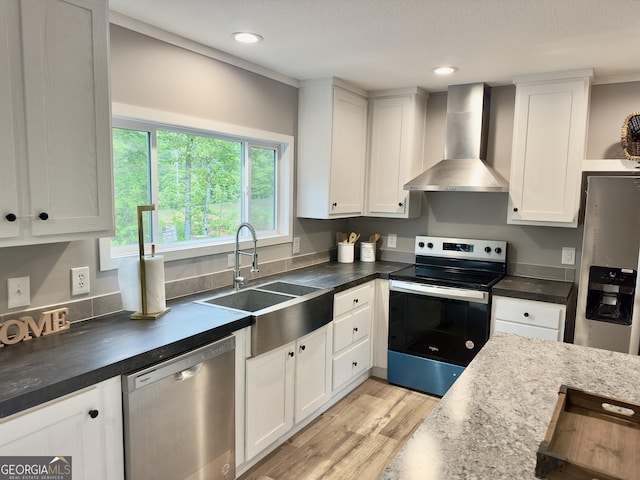 kitchen featuring wall chimney exhaust hood, stainless steel appliances, light wood-style flooring, white cabinetry, and a sink