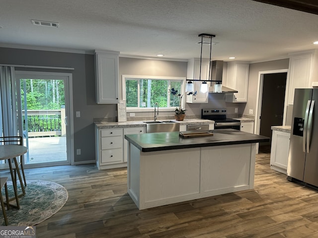 kitchen featuring stainless steel appliances, a sink, wall chimney exhaust hood, a center island, and white cabinetry