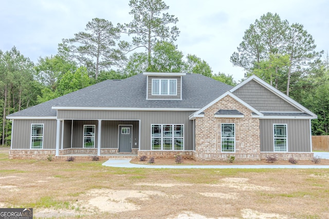 craftsman house with a shingled roof, covered porch, a front yard, brick siding, and board and batten siding