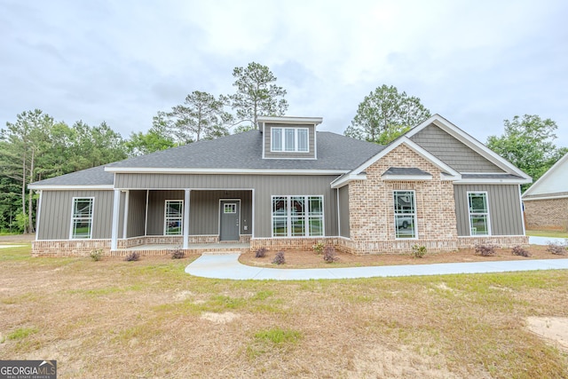view of front of house with covered porch, a shingled roof, and a front yard