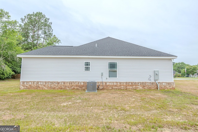 back of property with cooling unit, a lawn, roof with shingles, and brick siding