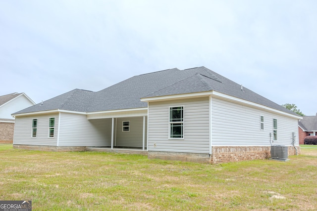 rear view of house with a lawn, cooling unit, and a shingled roof