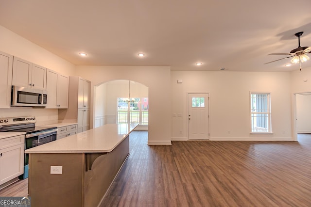kitchen with stainless steel appliances, arched walkways, open floor plan, dark wood-type flooring, and a kitchen island
