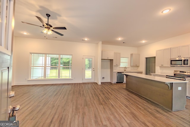kitchen with appliances with stainless steel finishes, a sink, light countertops, a kitchen island, and wood finished floors