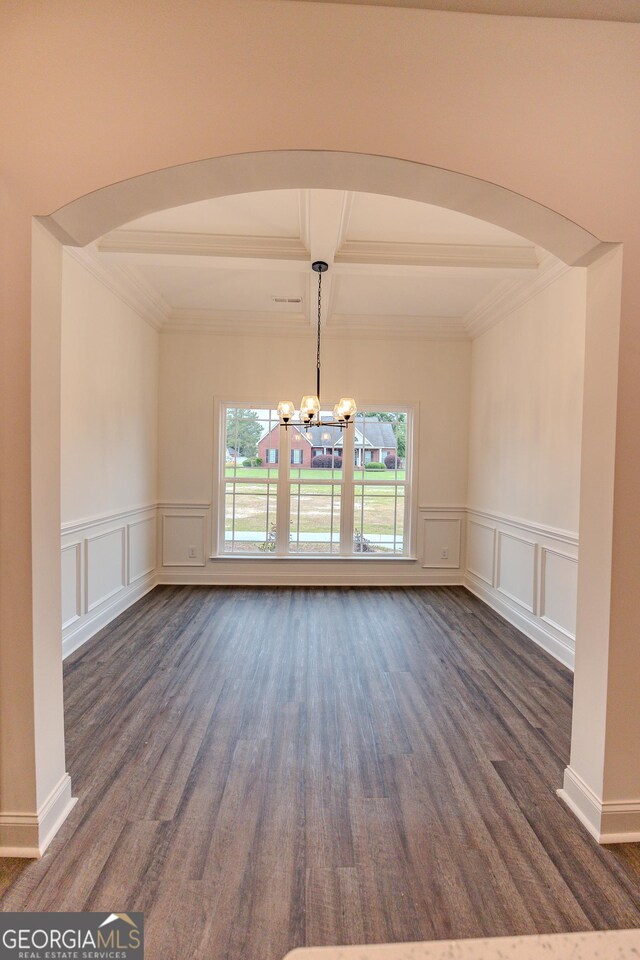 unfurnished dining area featuring a decorative wall, beamed ceiling, dark wood-type flooring, a chandelier, and ornamental molding