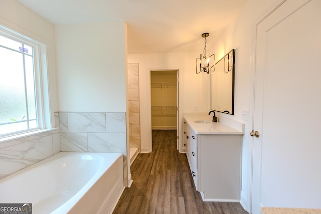 bathroom featuring a walk in closet, a chandelier, wood finished floors, a bath, and vanity