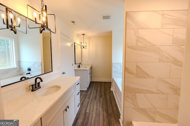 bathroom with a chandelier, two vanities, a tub to relax in, baseboards, and wood finished floors