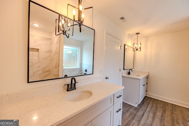 full bath featuring a chandelier, wood finished floors, two vanities, baseboards, and a tile shower