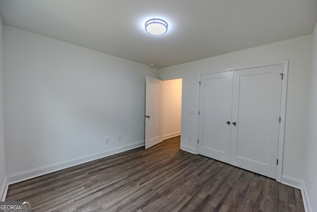 unfurnished bedroom with dark wood-style floors, baseboards, and a closet