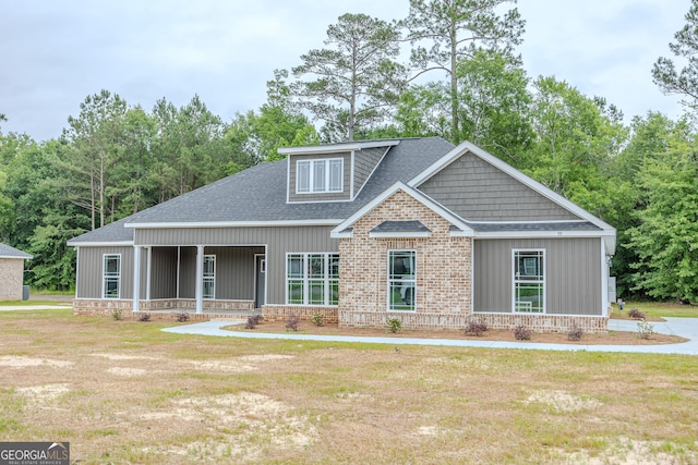 view of front facade with a shingled roof, a front yard, and brick siding