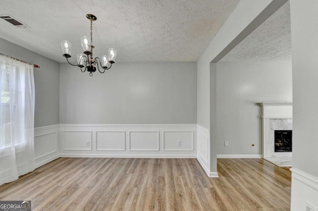 2355 Glen Chase Ln, Lawrenceville, GA 30044 - unfurnished dining area with a textured ceiling, a chandelier, light wood-style floors, a fireplace, and wainscoting