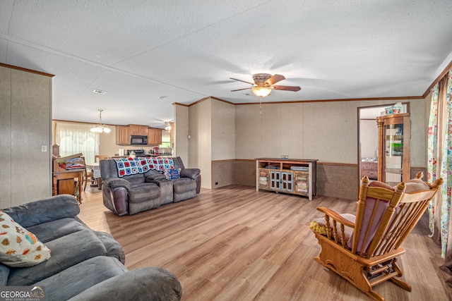 living room with light wood finished floors, ornamental molding, a ceiling fan, a textured ceiling, and a chandelier