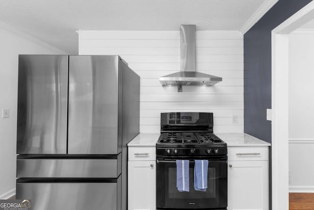 kitchen featuring freestanding refrigerator, black gas stove, wall chimney range hood, ornamental molding, and white cabinetry