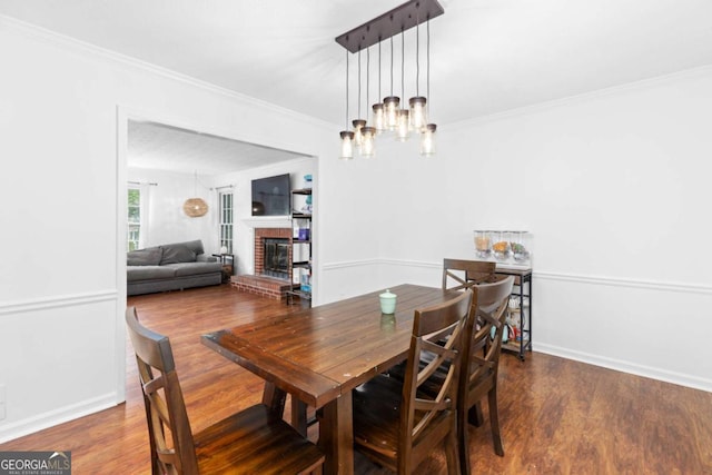 dining room featuring wood finished floors, a fireplace, ornamental molding, a chandelier, and baseboards