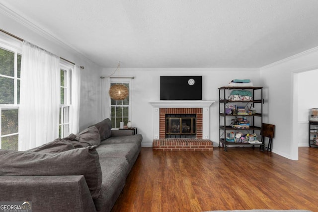 living room with a brick fireplace, wood finished floors, ornamental molding, baseboards, and a textured ceiling