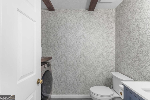 bathroom with washer / dryer, beamed ceiling, toilet, and vanity