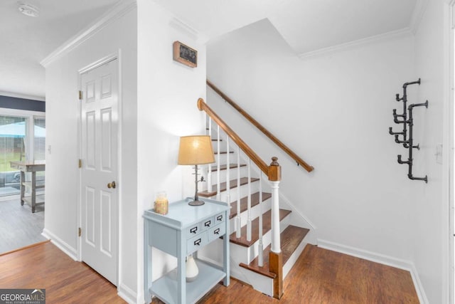 staircase with wood finished floors, ornamental molding, and baseboards