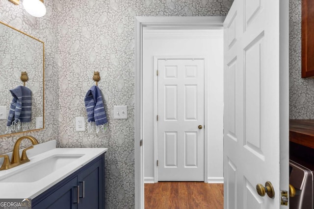 bathroom with wallpapered walls, wood finished floors, and vanity