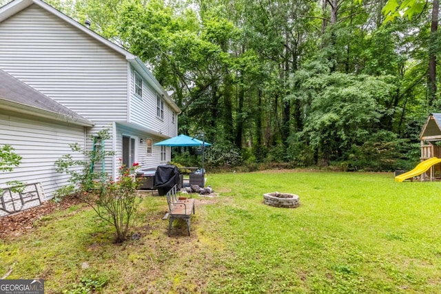 view of grassy yard with an outdoor fire pit and a playground