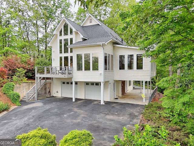 view of front of property with stairway, asphalt driveway, an attached garage, roof with shingles, and a deck