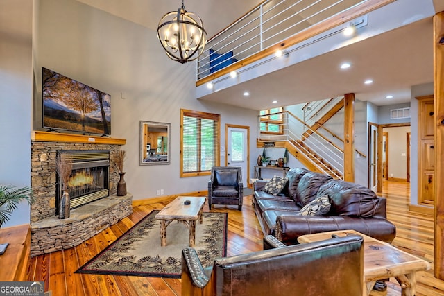 living room featuring stairway, a chandelier, a stone fireplace, hardwood / wood-style floors, and a towering ceiling