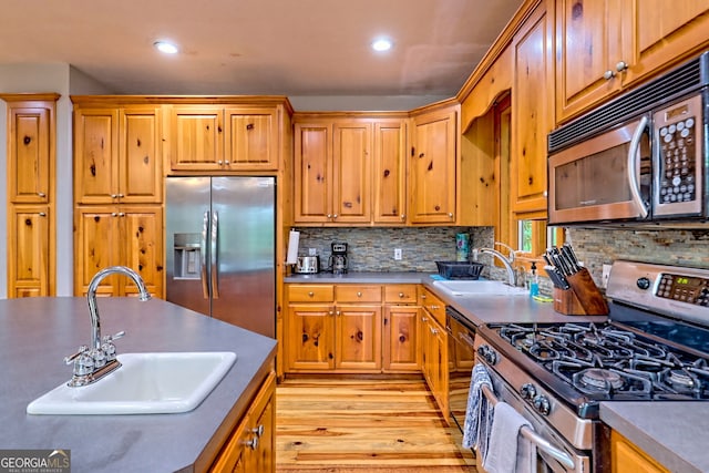 kitchen with stainless steel appliances, a sink, light wood finished floors, recessed lighting, and backsplash