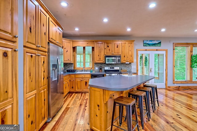 kitchen with appliances with stainless steel finishes, light wood-type flooring, decorative backsplash, a breakfast bar, and recessed lighting