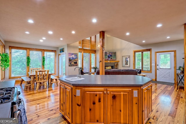 kitchen with a sink, dark countertops, a center island with sink, stainless steel gas stove, and light wood-style floors