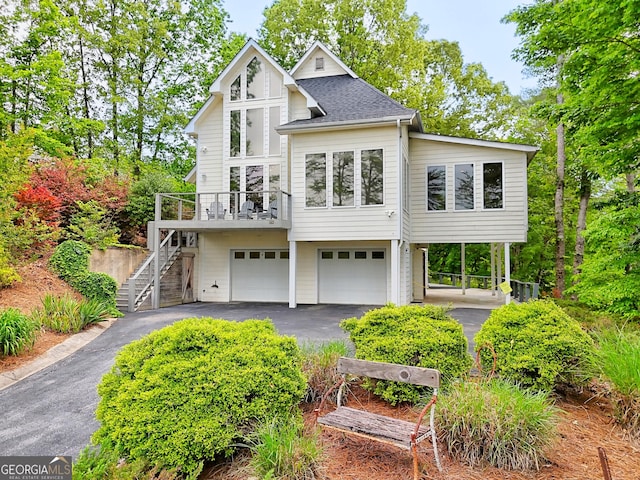 view of front of house featuring asphalt driveway, an attached garage, stairs, and roof with shingles