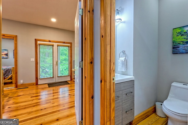 bathroom featuring wood finished floors, toilet, vanity, baseboards, and recessed lighting