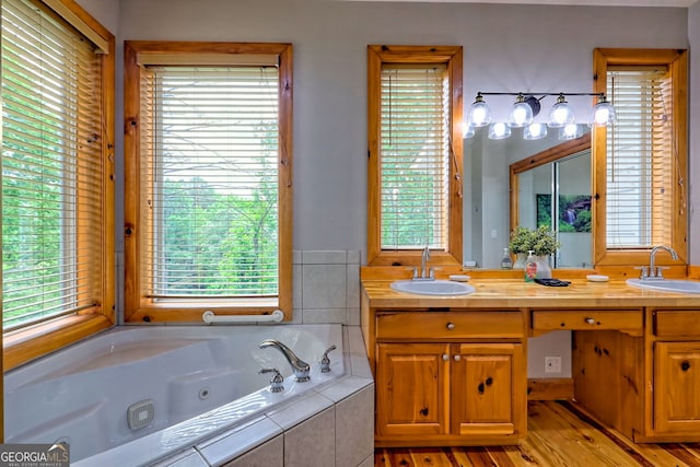 bathroom with a jetted tub, double vanity, and wood finished floors