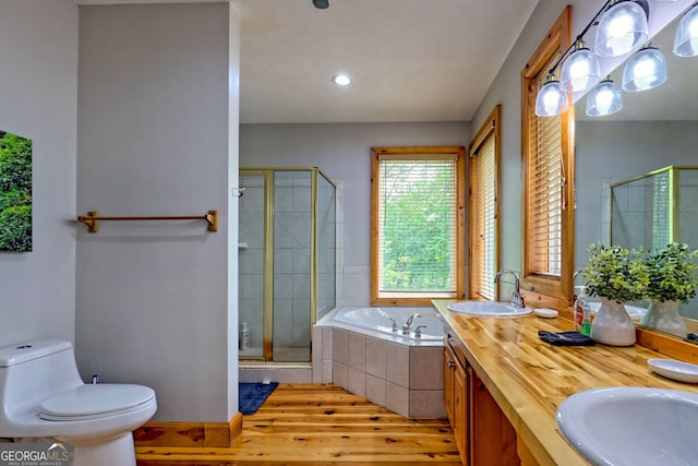 bathroom featuring wood finished floors, a stall shower, a bath, toilet, and double vanity