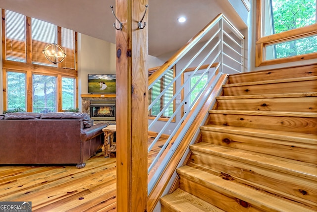 stairway featuring wood finished floors, a chandelier, a fireplace, and recessed lighting