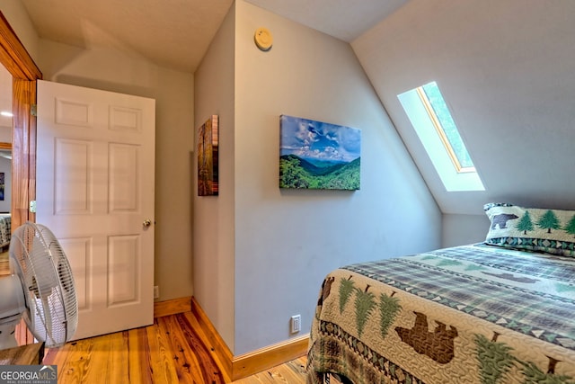 bedroom featuring a skylight, vaulted ceiling, light wood-style floors, and baseboards