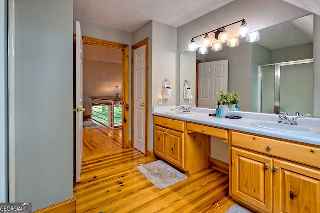 bathroom featuring wood finished floors, double vanity, and a stall shower