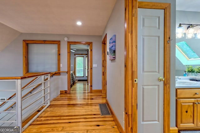 hall with light wood-style flooring, a sink, recessed lighting, a skylight, and baseboards