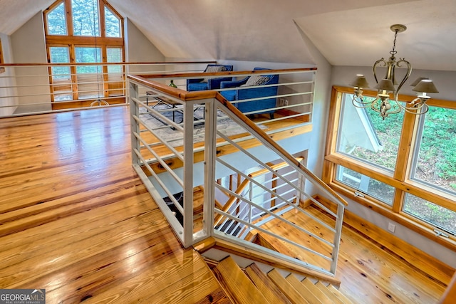 stairway with a chandelier, vaulted ceiling, and hardwood / wood-style flooring