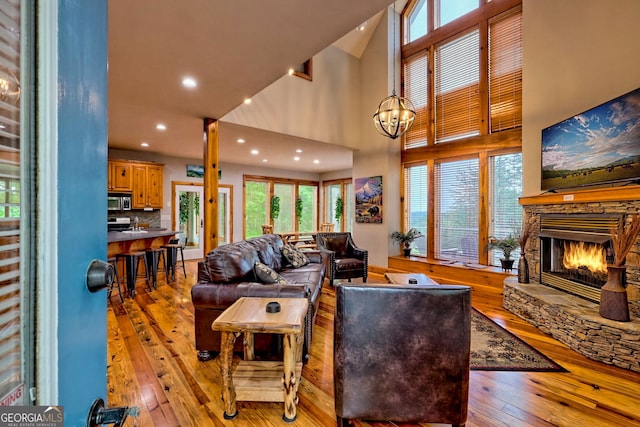 living room featuring light wood finished floors, a stone fireplace, a towering ceiling, healthy amount of natural light, and recessed lighting