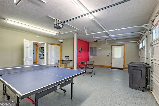 rec room featuring a garage, a textured ceiling, electric panel, and baseboards