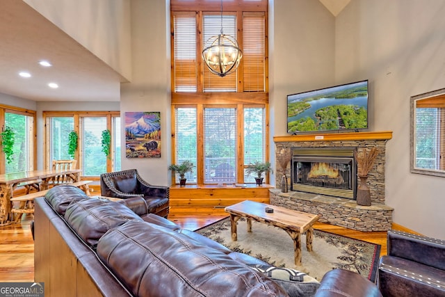 living area with wood finished floors, a high ceiling, a chandelier, a stone fireplace, and recessed lighting